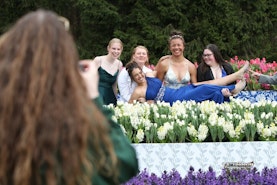 Photo of 5 girls celebrating homecoming with a silly pose surrounded by waist-high white tulips, pink tulips, and purple hyacinths.