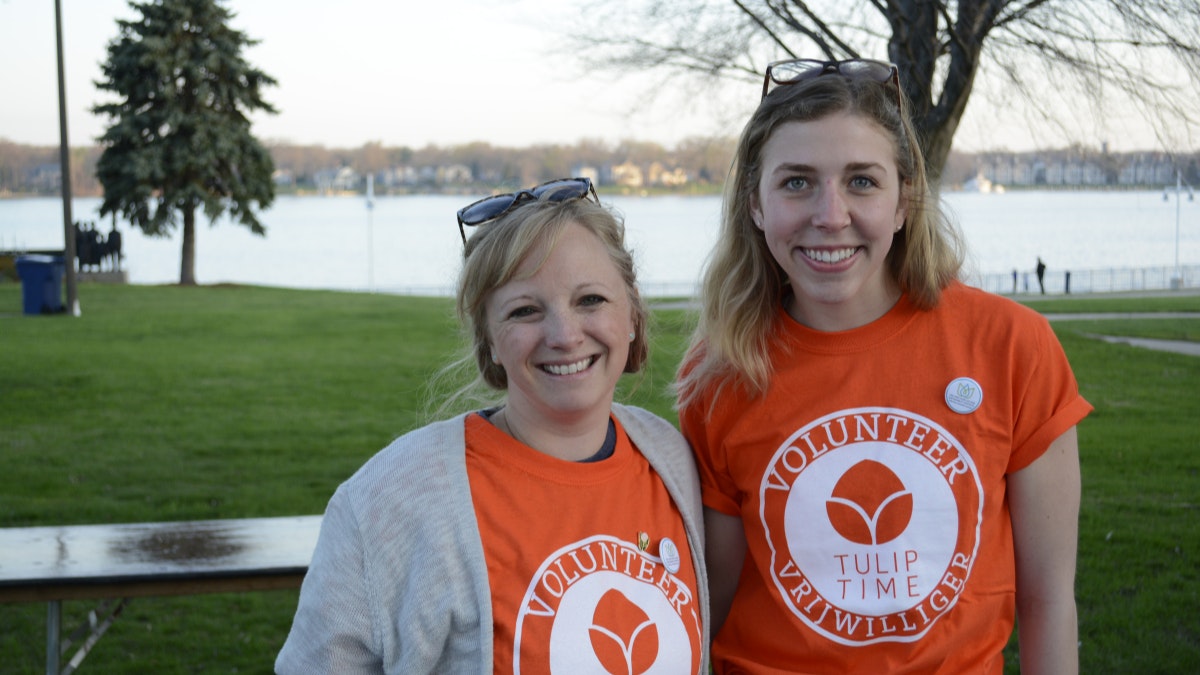 Two women smiling while wearing their Tulip Time volunteer shirts at Kollen Park on a beautiful day.